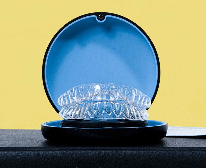 A clear braces with a blue case is lain on top of a yellow background.