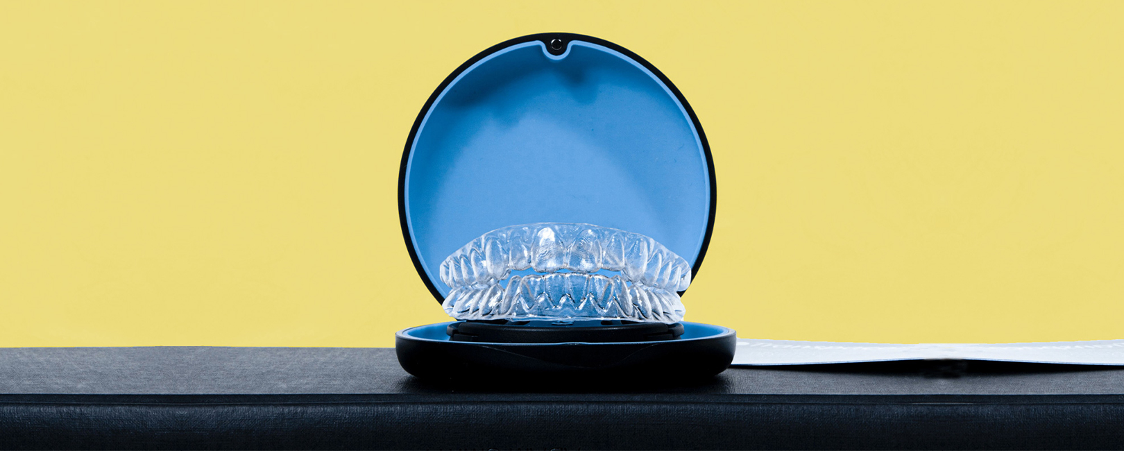 A clear braces with a blue case is lain on top of a yellow background.