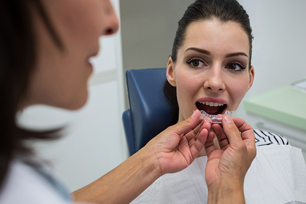 A dentist is putting a transparent aligner in a woman’s mouth.