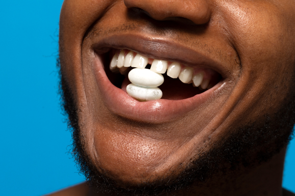 A man with gaps between his teeth is smiling with a candy in his mouth