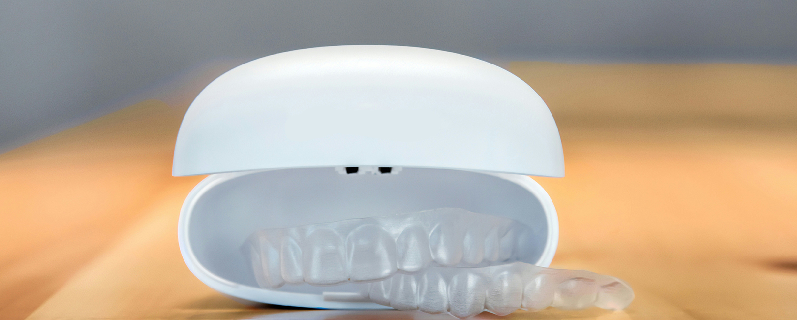 A white braces case with a clear transparent braces in it lain on a wooden table.
