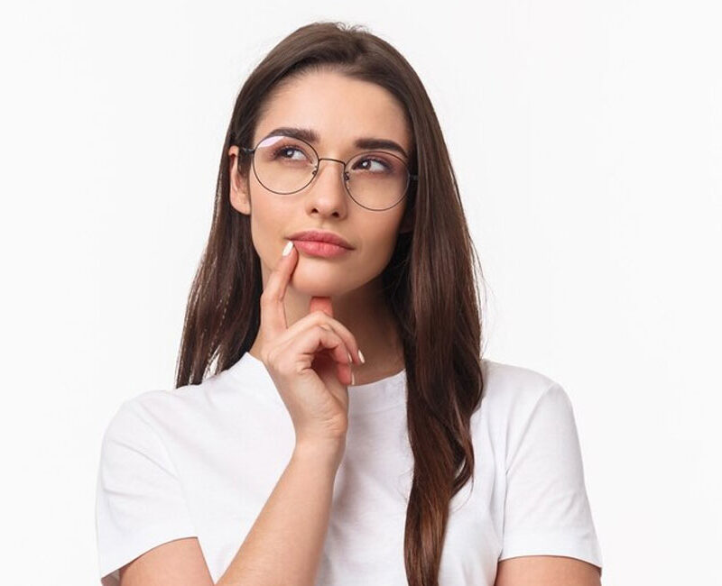 A young woman wearing glasses is thinking about the effects of clear aligners on teeth alignment.