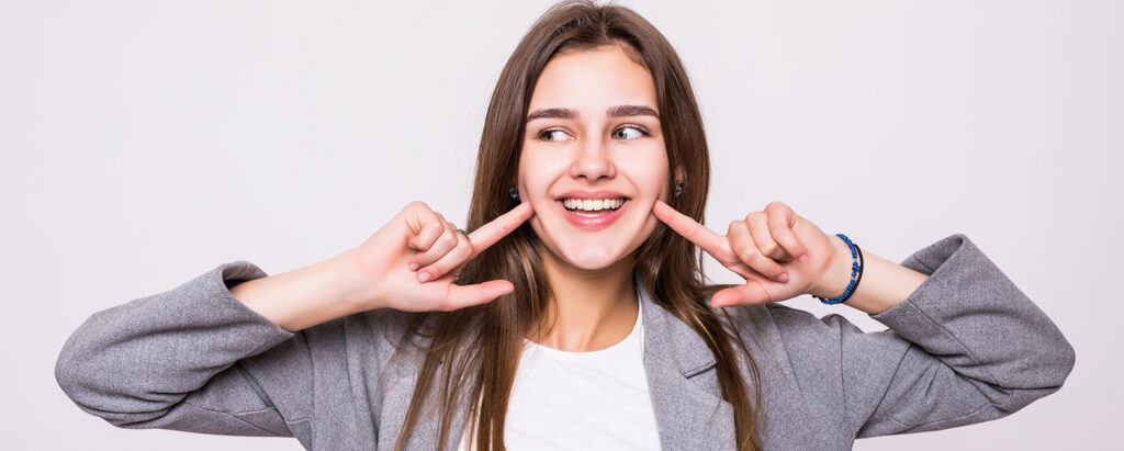 A young woman is making a face with her hands, showcasing a confident smile achieved through professional tips for straightening her teeth.