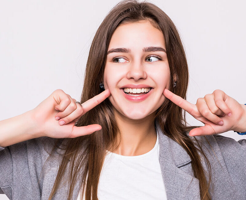 A young woman is making a face with her hands, showcasing a confident smile achieved through professional tips for straightening her teeth.