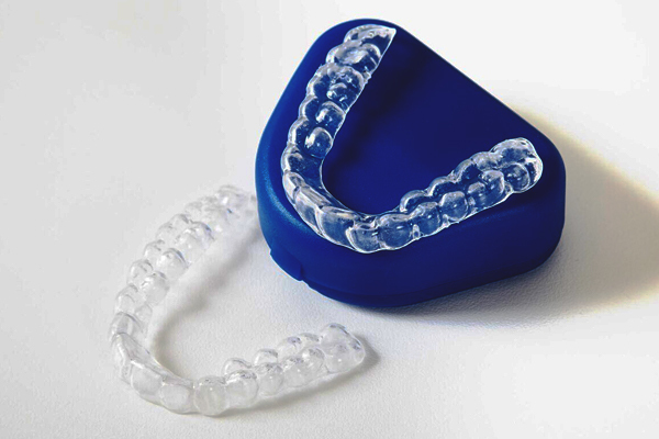 Clear aligners next to their blue storage case on a white background.