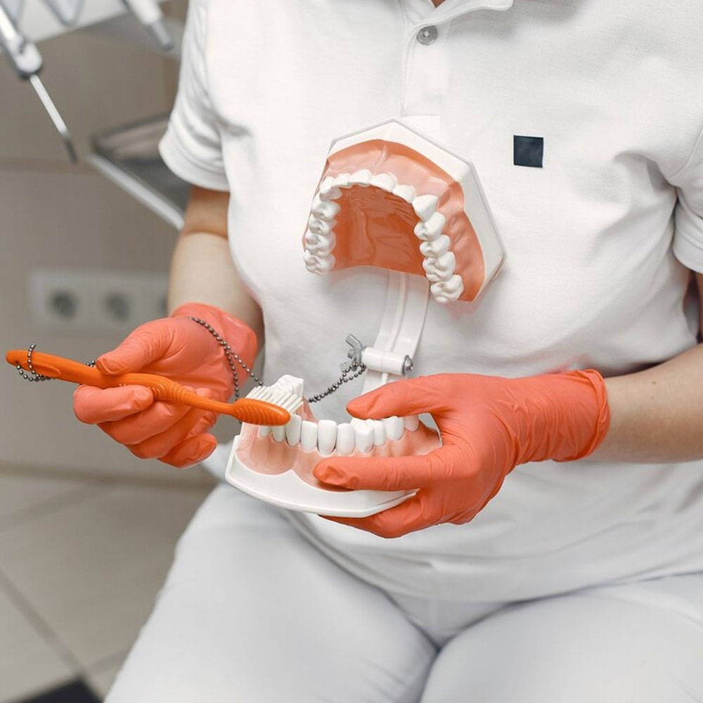 Dental professional in orange gloves demonstrating proper tooth brushing technique.