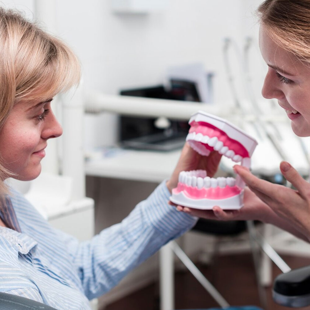 A woman is showing a clear aligner treatment process model to another woman.