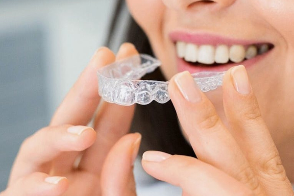 A woman is holding a clear invisible aligner in her hands.