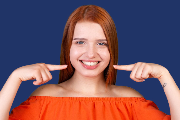 Woman with red hair smiling and pointing to her cheeks, showcasing her clear aligners.