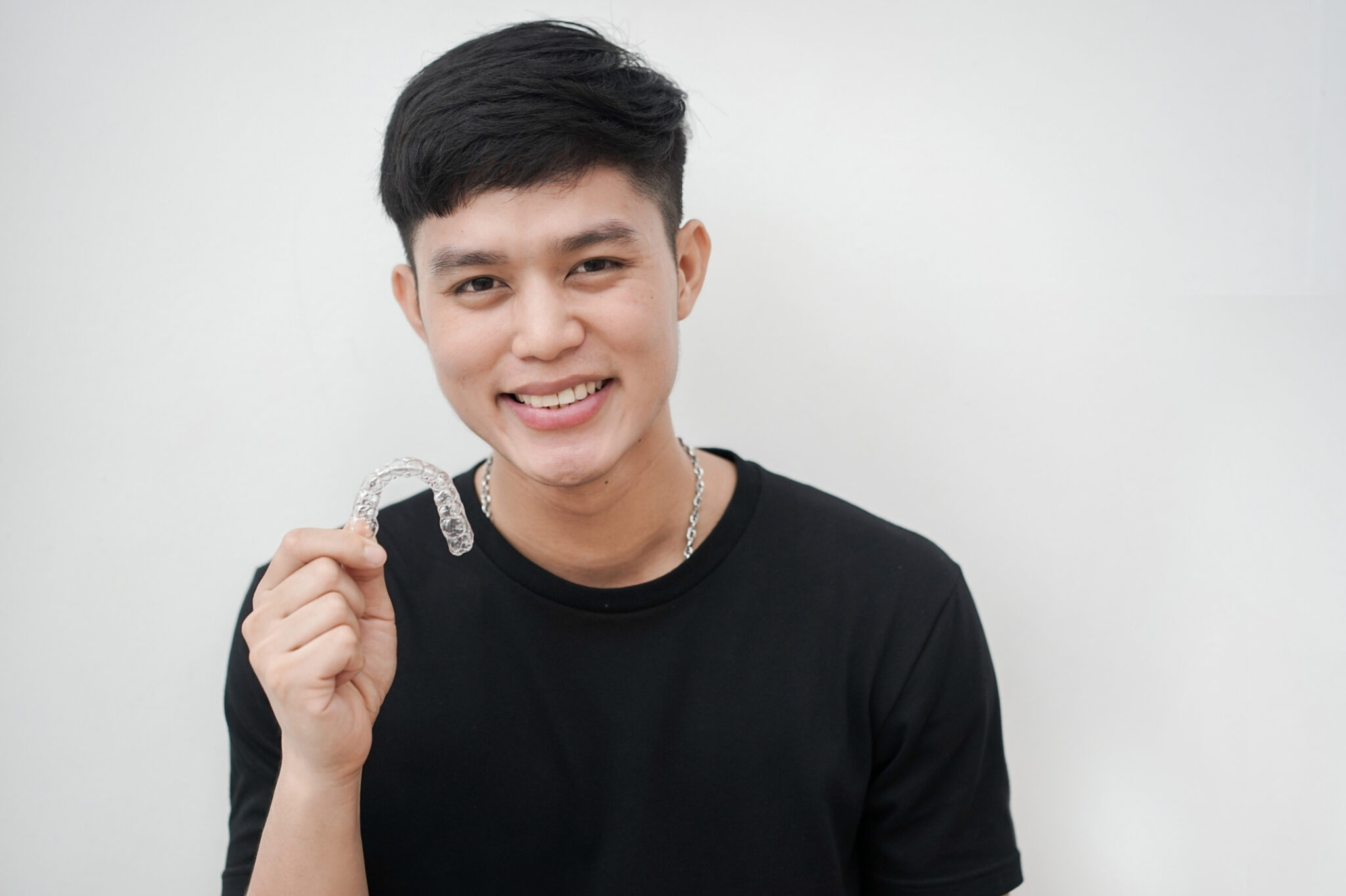 A young man holding a pair of clear aligner trays for teeth whitening treatment.
