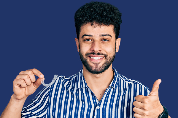 Man smiling while holding clear aligners and giving a thumbs-up.