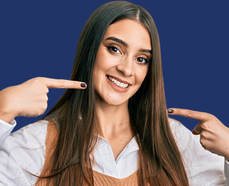 A smiling woman pointing to her clear aligners.