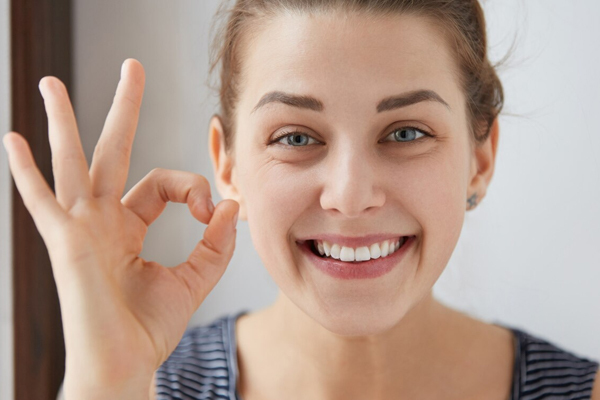 A smiling woman with clear aligners making an ok hand gesture.