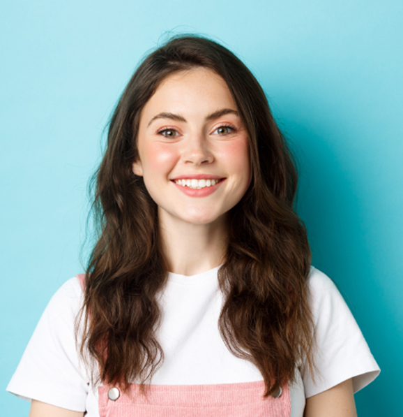 A smiling young woman wearing clear aligners against a blue background.