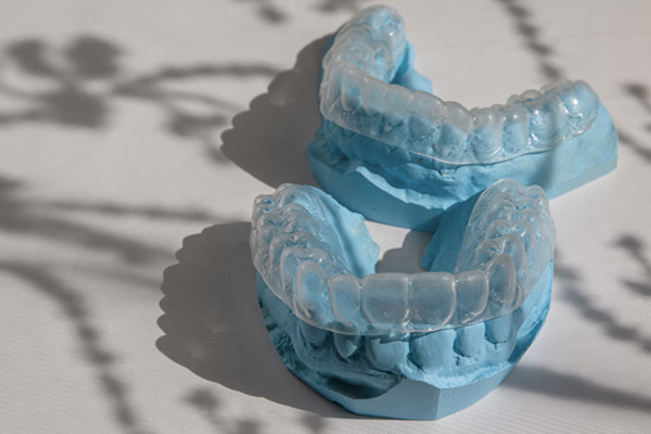 Clear aligners on a blue dental mold casting shadows on a white surface.
