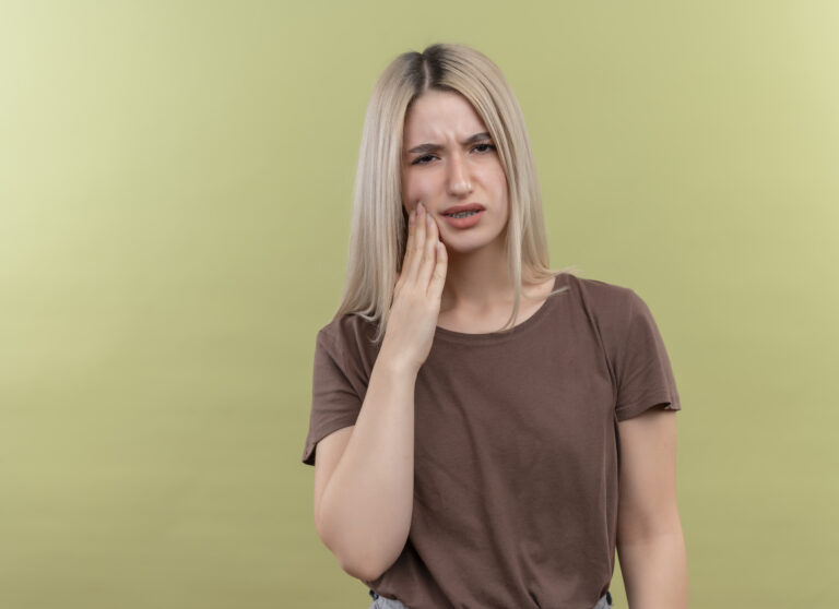 A woman with overcrowded teeth experiencing a toothache on a green background