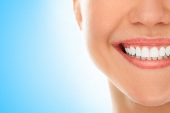 A woman smiles with a bright smile, showcasing her perfectly aligned teeth on a blue background.
